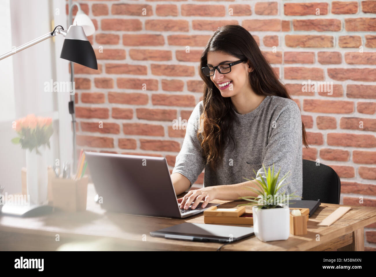 Young Smiling Woman Using Laptop On Office Desk Banque D'Images
