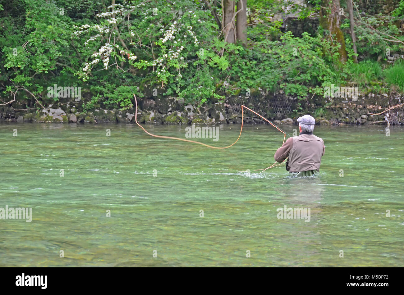 Un pêcheur à la mouche jette une voler à travers un swift river vers l'extrême-bank, en pataugeant dans l'eau profonde Banque D'Images