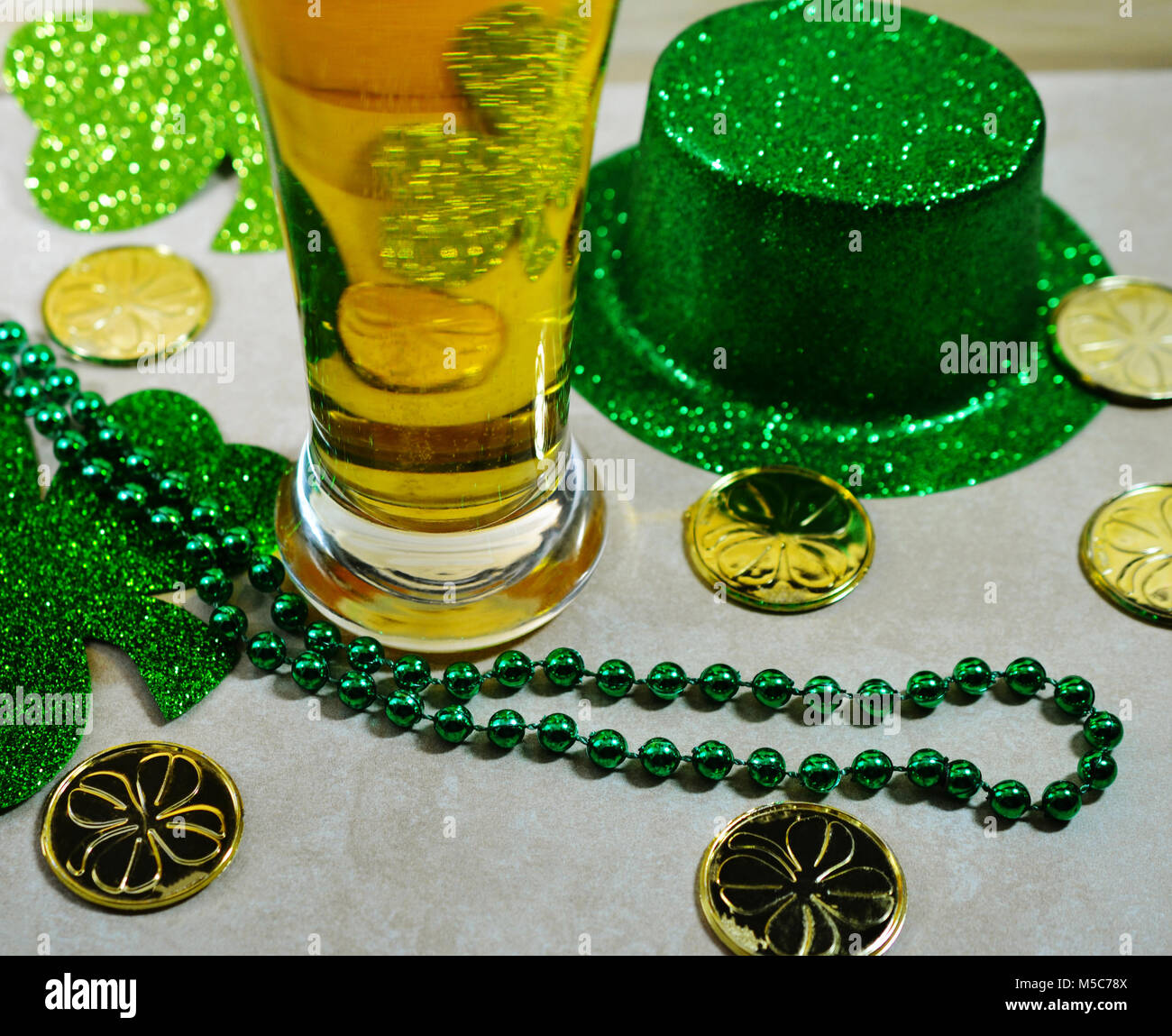 St Patricks Day Stein de bière en verre rempli de bière. Pas de mousse. Vert irlandais Top Hat, des pièces d'Or, perles vert, fond clair. Banque D'Images