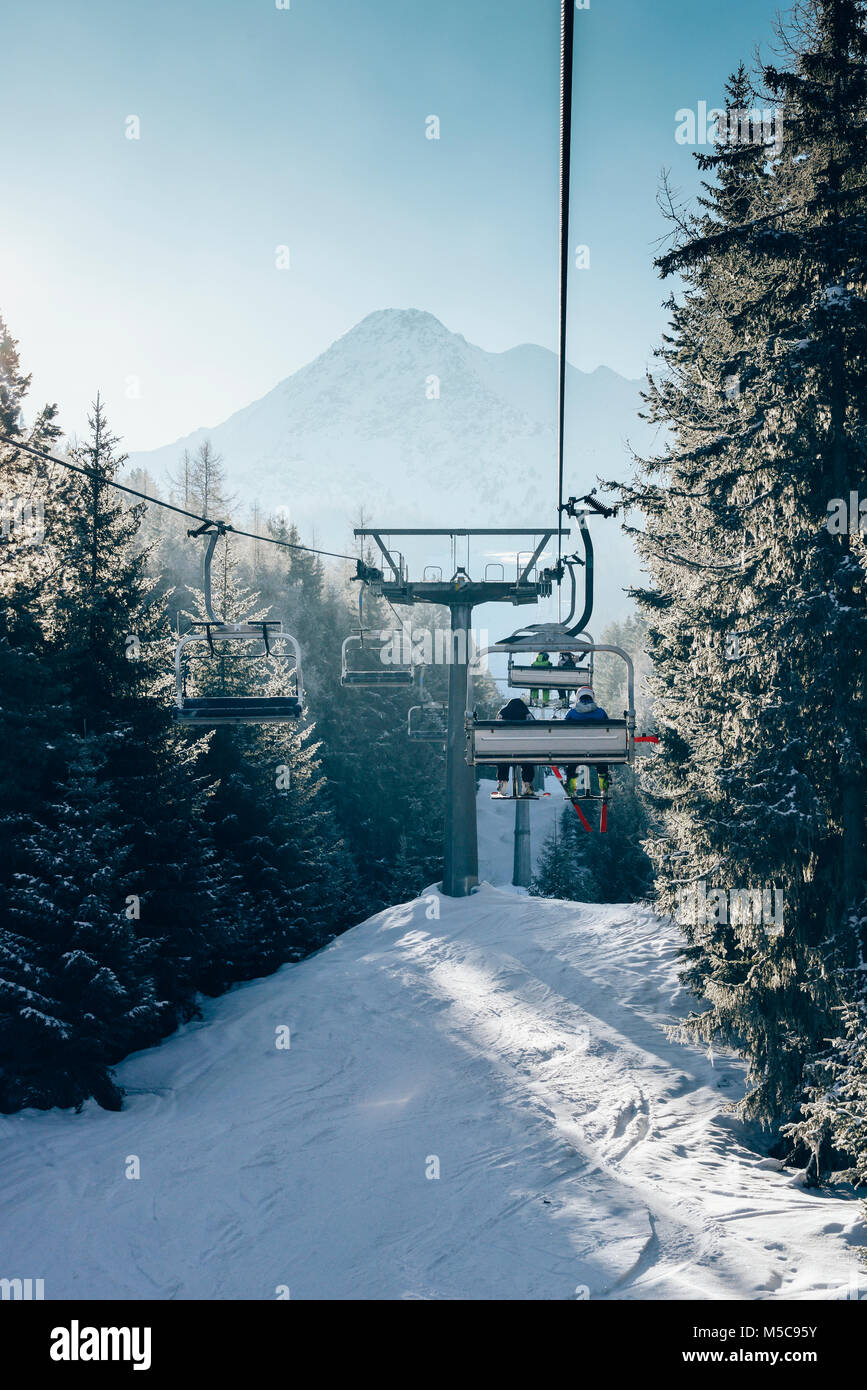 Soleil à travers les pins comme à l'ascension du télésiège de ski italienne recouvert de neige - concept de sports d'hiver Banque D'Images