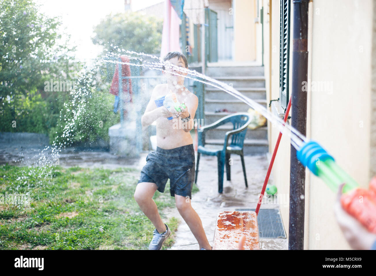 Les enfants jouent dans le jardin avec des fusils et carabines de l'eau sur une journée ensoleillée ayant beaucoup de plaisir Banque D'Images