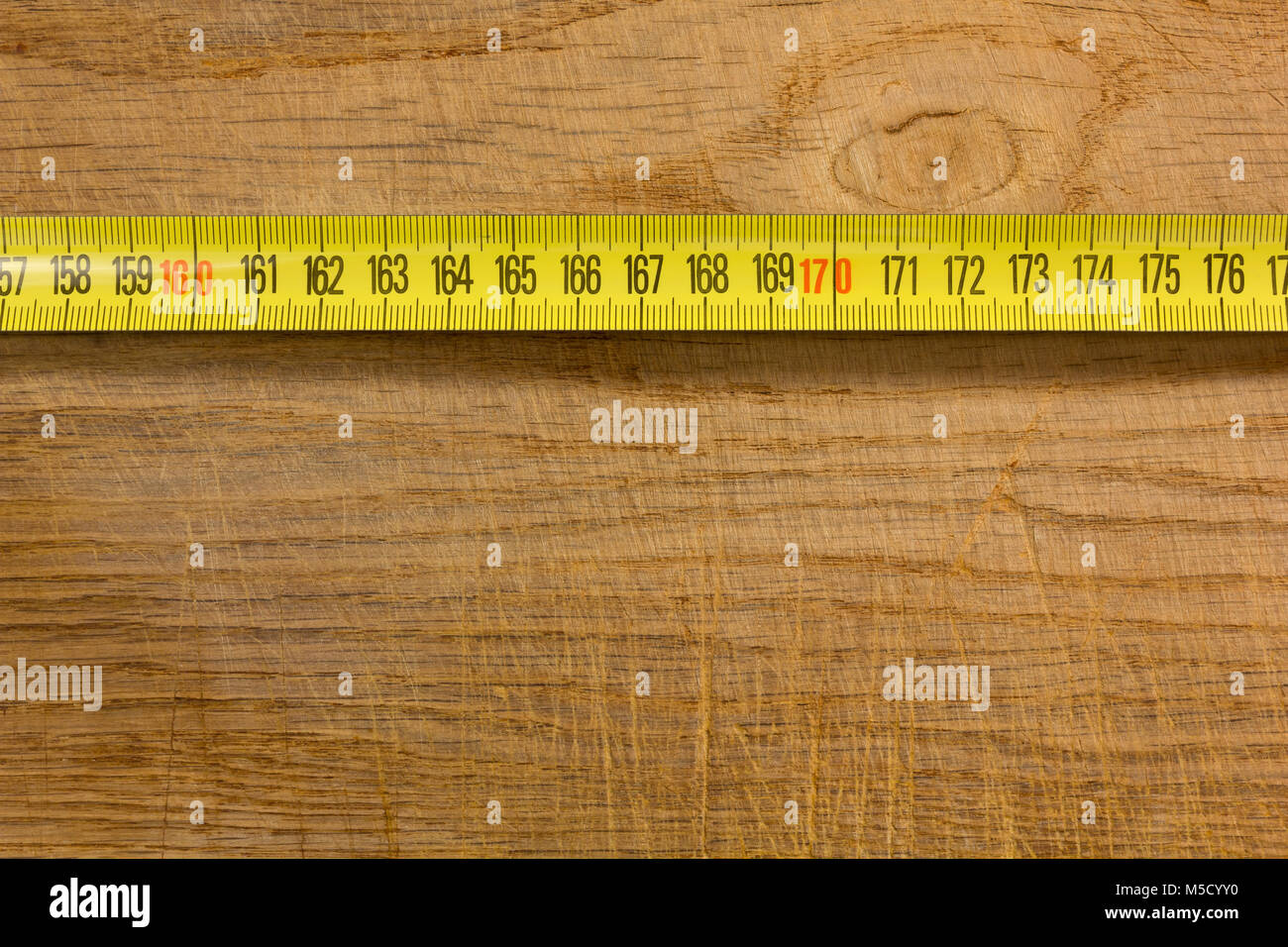 Segment d'un ruban à mesurer en métal jaune placé à l'horizontale sur une vieille table en bois Banque D'Images