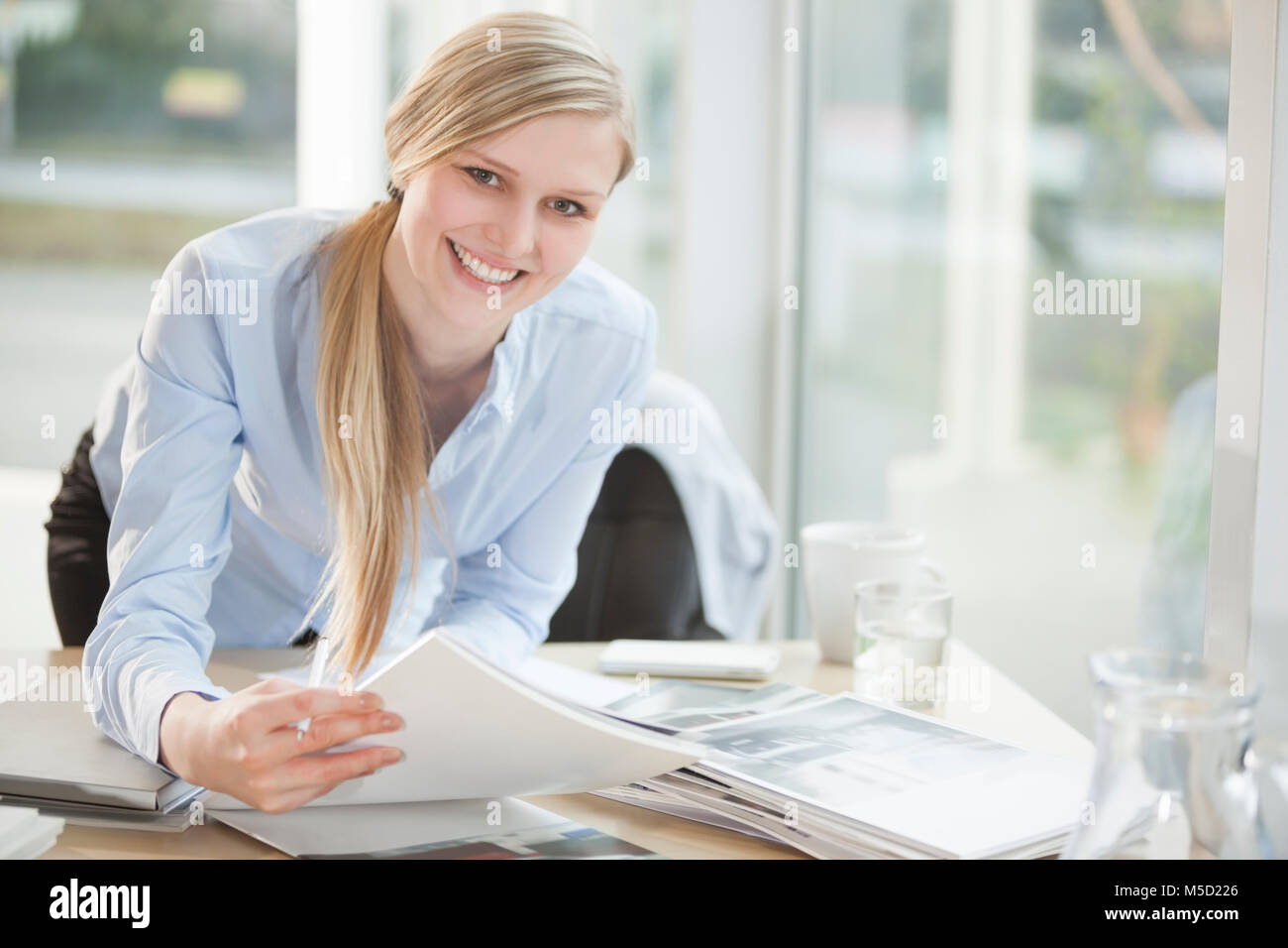 Portrait of happy young businesswoman with paperwork at desk in office Banque D'Images