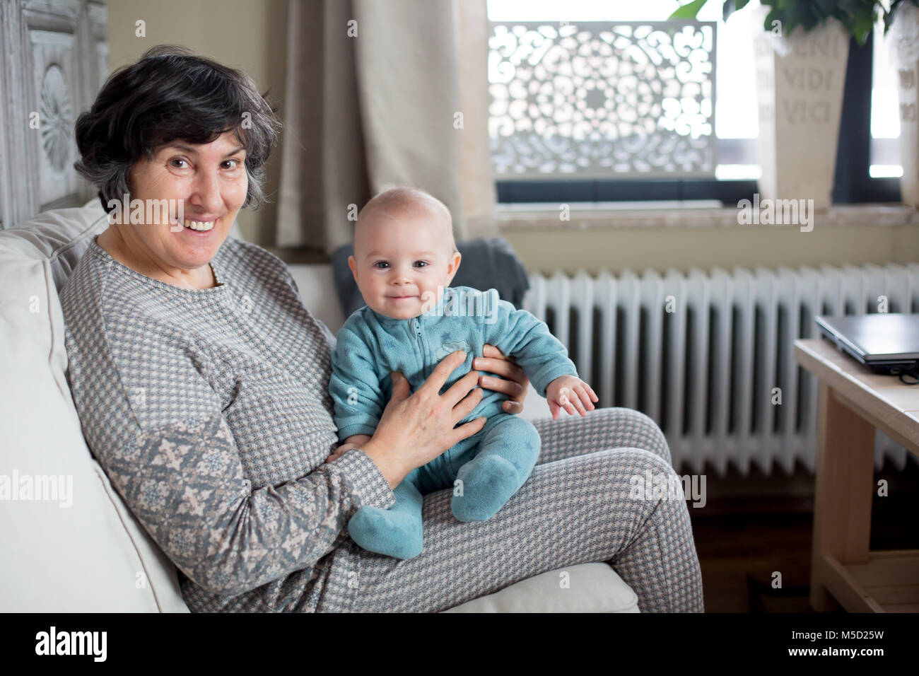Grand-mère tenant peu bébé garçon, assis dans un salon confortable avec beaucoup de lumière naturelle Banque D'Images