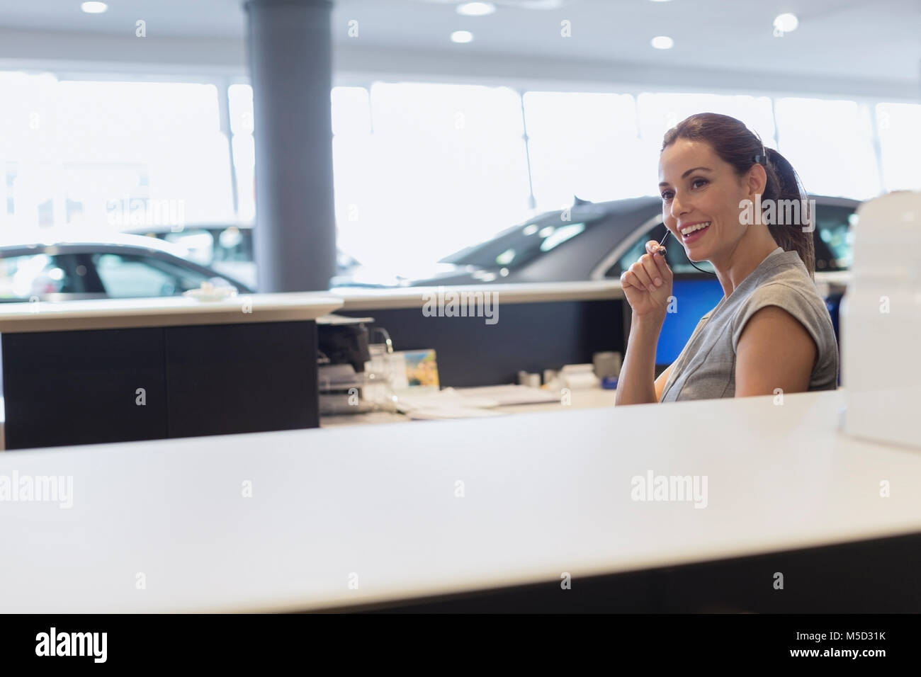 Réceptionniste femme de parler sur l'appareil mains libres de téléphone dans car dealership showroom Banque D'Images