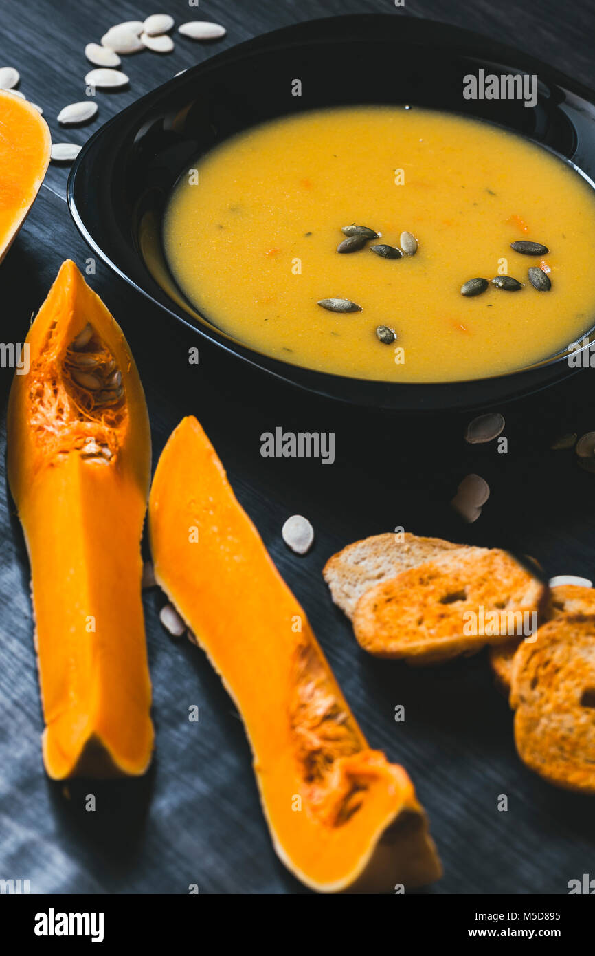 Soupe au potiron avec des tranches de citrouille fraîche sur un côté. Fond en bois foncé Banque D'Images