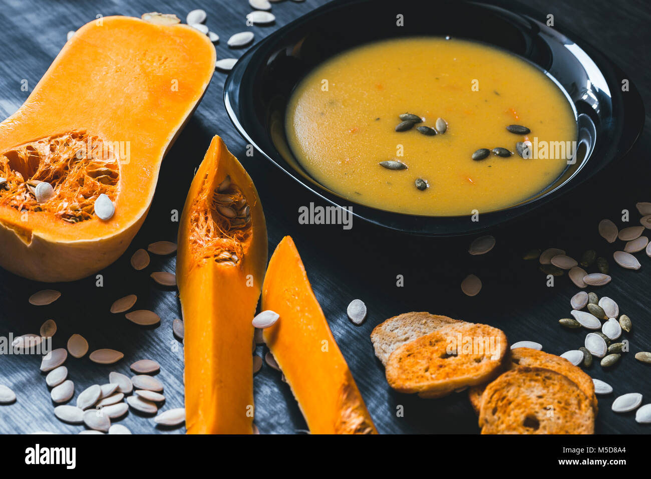 Soupe au potiron avec des tranches de citrouille fraîche sur un côté. Fond en bois foncé Banque D'Images