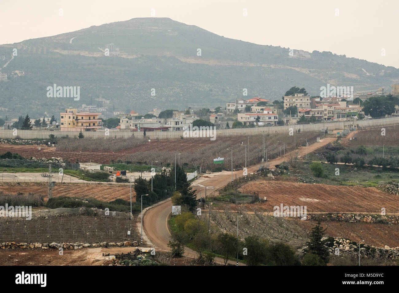 Metula, Israël. 21 Février, 2018. Vue de Metula, au premier plan, ses zones agricoles dans le milieu de terrain, le mur frontière inachevée et le Liban dans l'arrière-plan. Au cours de la guerre du Liban de 2006, Metula est devenue une ville fantôme comme sa population fui pour échapper temporairement à la roquette du Hezbollah. La ville a été touchée par des roquettes 120 pendant la guerre. Les efforts de la diplomatie pour résoudre les tensions entre Israël et le Liban sont en cours avec la médiation de l'État américain du Ministère Satterfield. Les différends sur la frontière israélienne construction d'un mur, le début de l'exploration de gaz en mer et les Banque D'Images