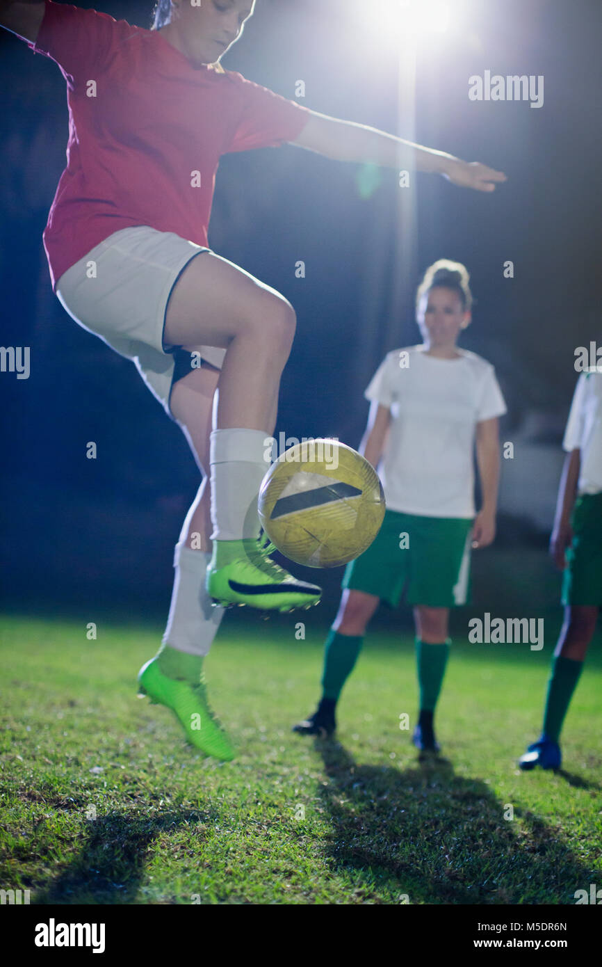 Jeune joueur de soccer féminin, pratiquant le saut et des coups de la balle sur la nuit sur le terrain Banque D'Images