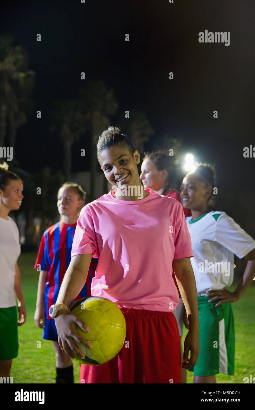 Portrait souriant et confiant avec le joueur de soccer féminin balle sur domaine de nuit Banque D'Images