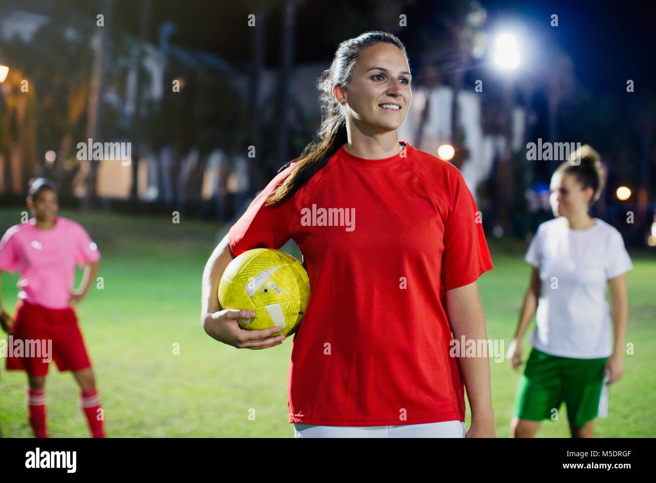 Portrait de confiance, souriante jeune femme joueur de football sur terrain de nuit Banque D'Images