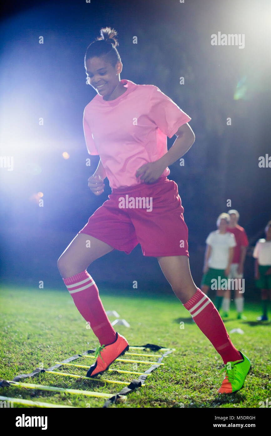 Les jeunes joueuses de soccer la pratique de sports d'agilité sur terrain de forage dans la nuit Banque D'Images