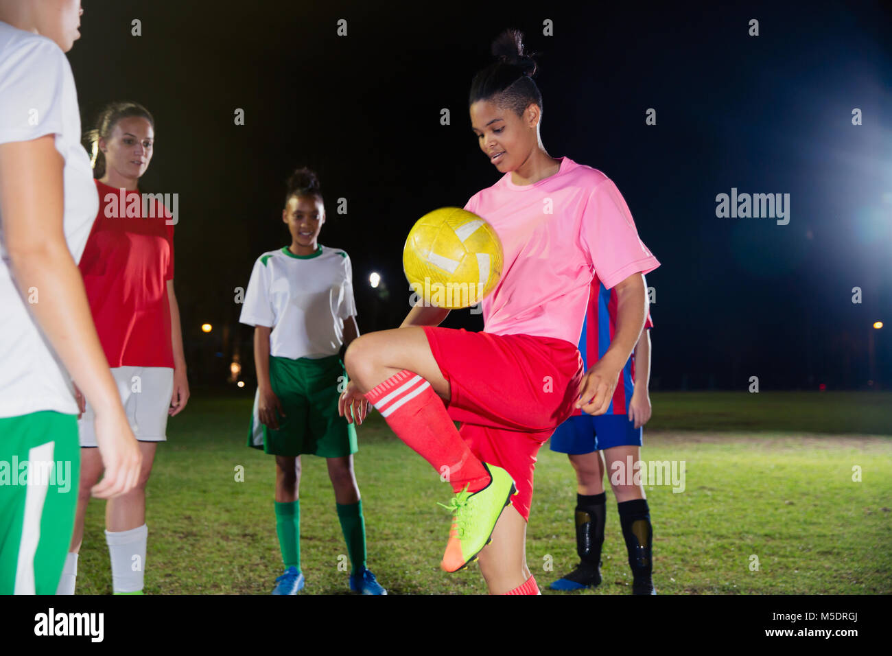 Jeune joueur de soccer féminin pratiquant, balle qui rebondit sur le genou de nuit sur le terrain Banque D'Images