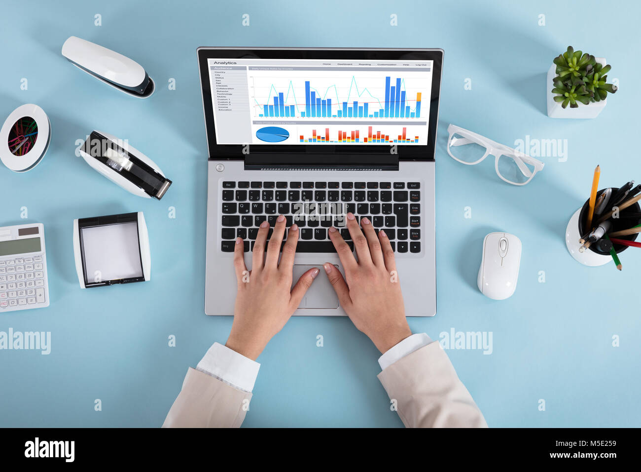 Close-up of a Businesswoman analyser divers graphiques sur ordinateur portable sur Blue Desk In Office Banque D'Images