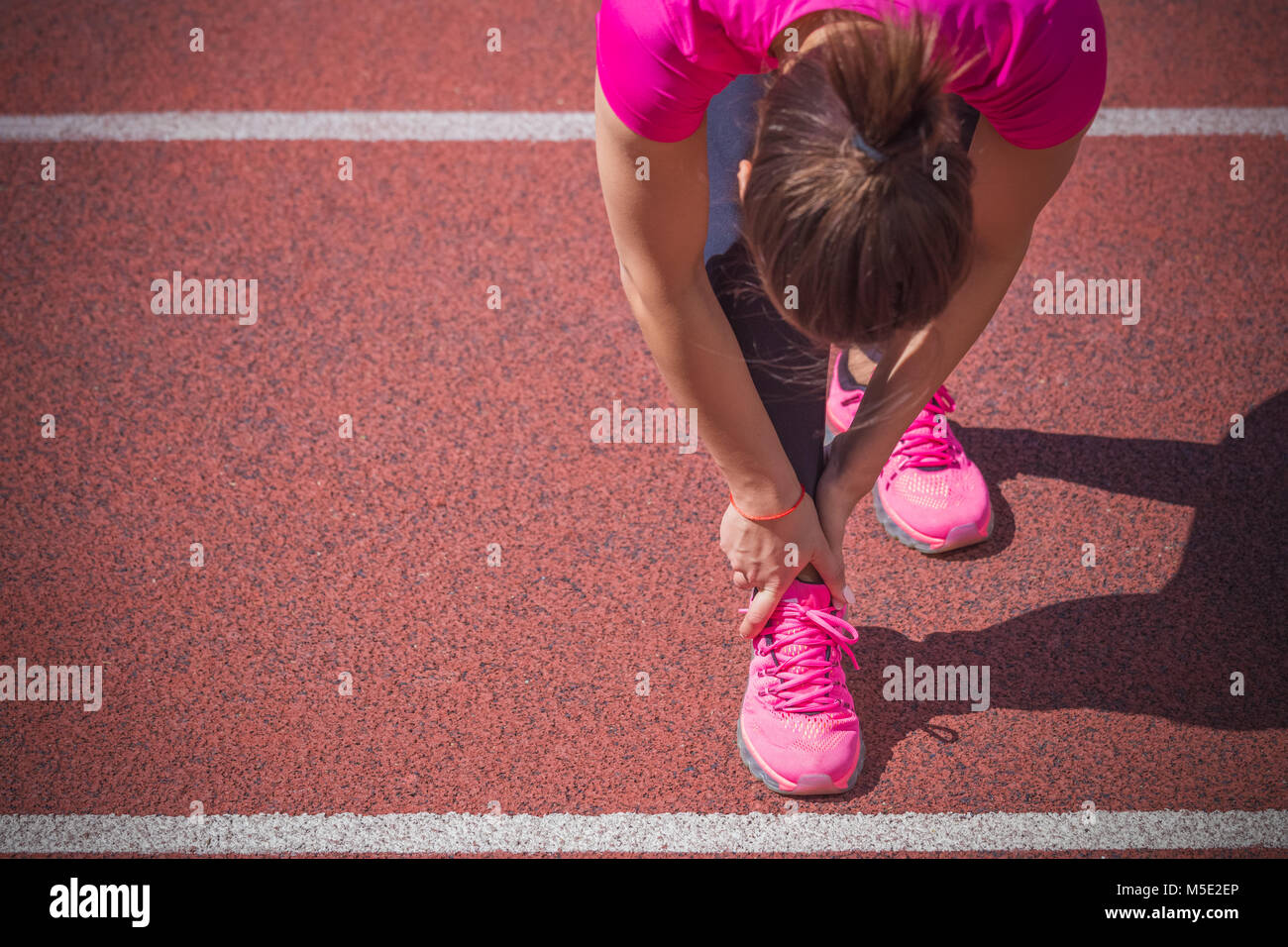 Female jogger mains sur pied. Elle ressent la douleur comme la cheville ou le pied est cassé ou tordu. Accident sur une piste de course au cours de l'exercice matinal. Spo Banque D'Images
