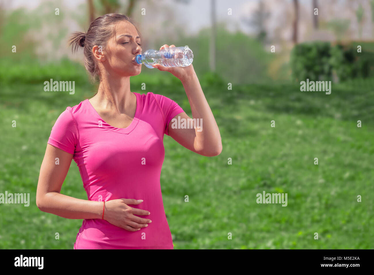 Runner Fitness Femme de l'eau potable dans le parc. Fille de l'athlète en faisant une pause pendant l'exécution d'hydrater pendant les chaudes journées d'été. Mode de vie sain et actif. Banque D'Images