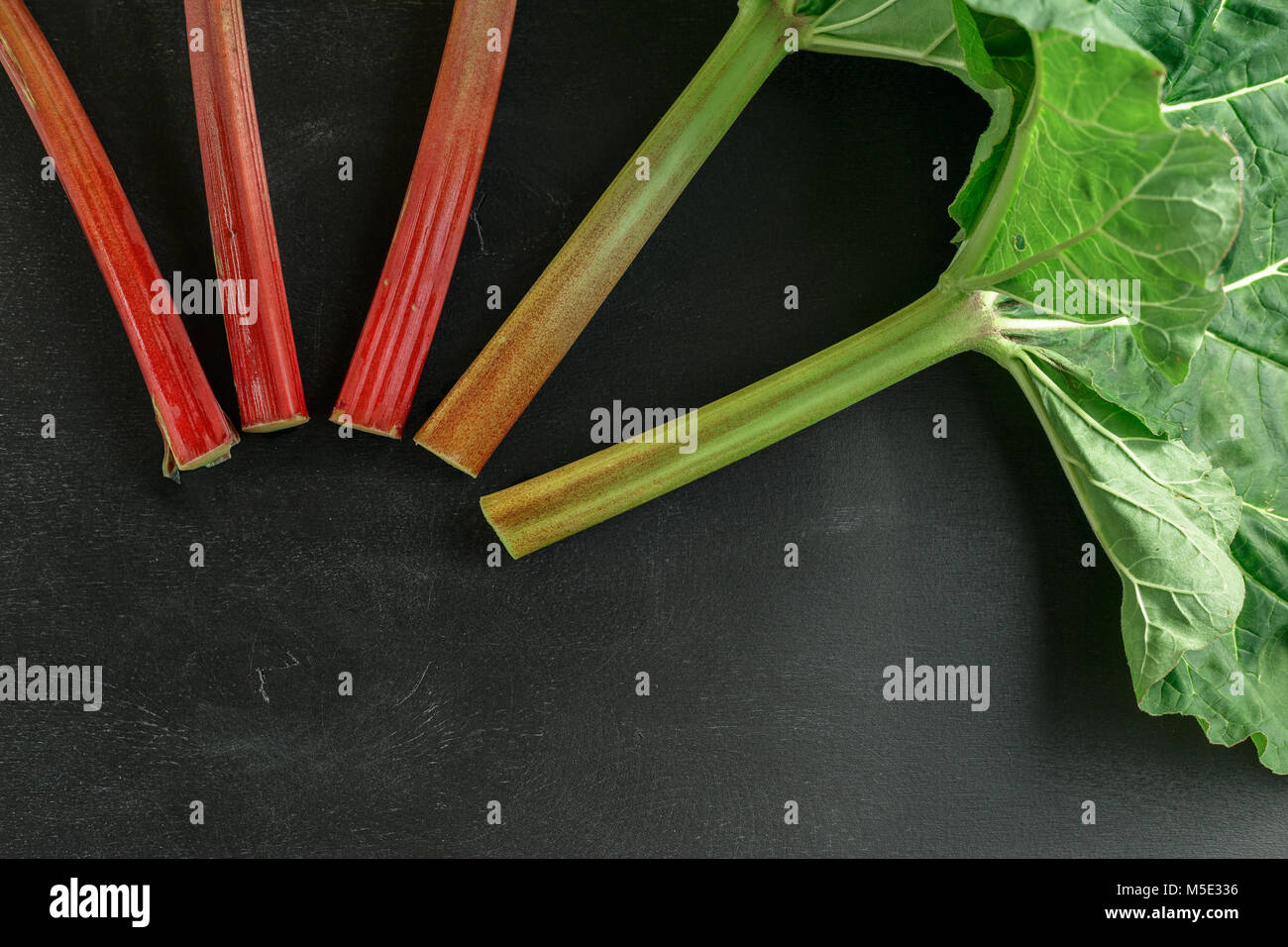 Tiges de rhubarbe fraîche bio avec des feuilles sur tableau noir fond de bois Banque D'Images