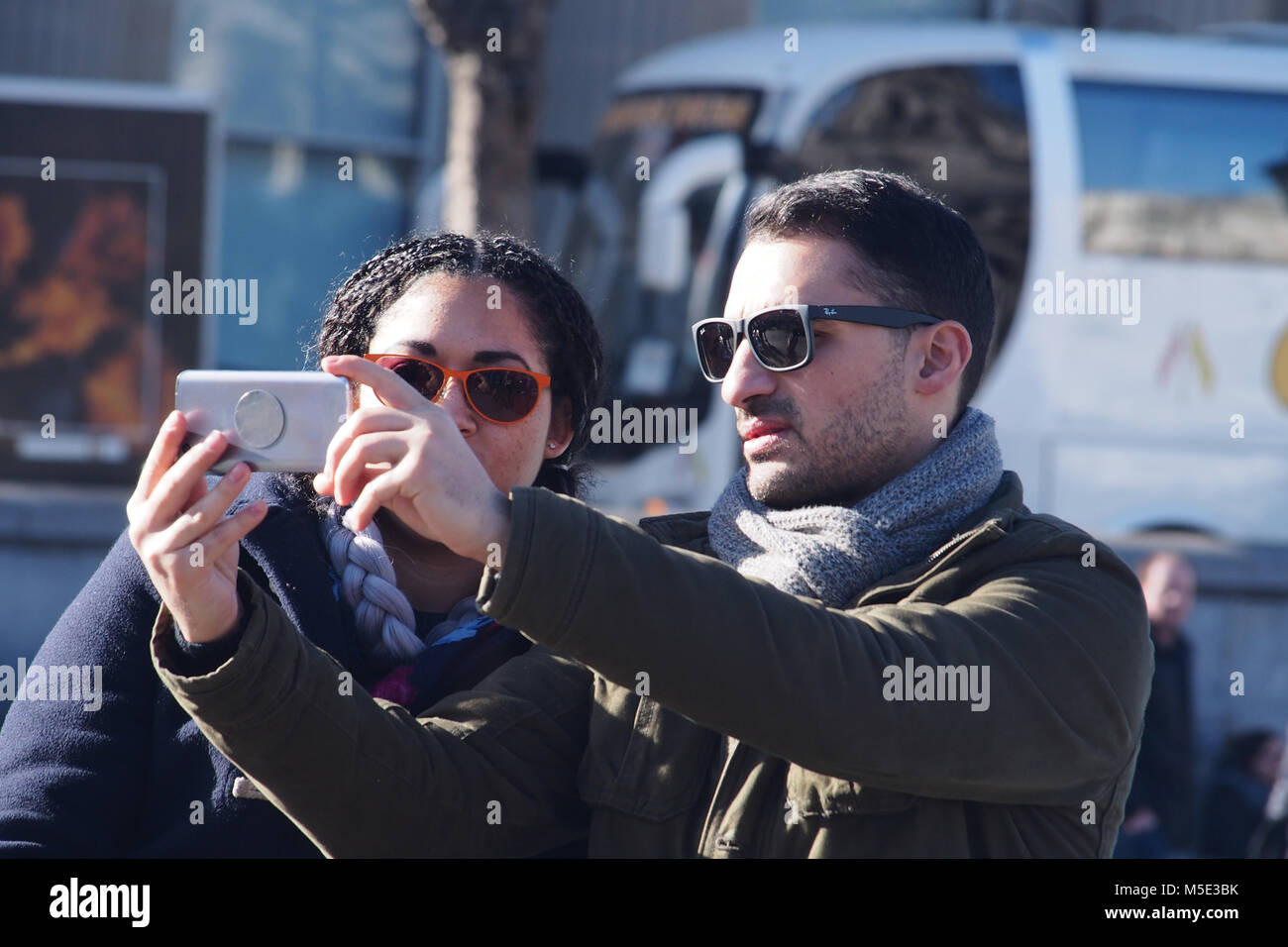Un jeune couple de prendre un avec un smartphone selfies portant des lunettes de soleil en hiver à Trafalgar Square, Londres, portant des vêtements d'hiver Banque D'Images