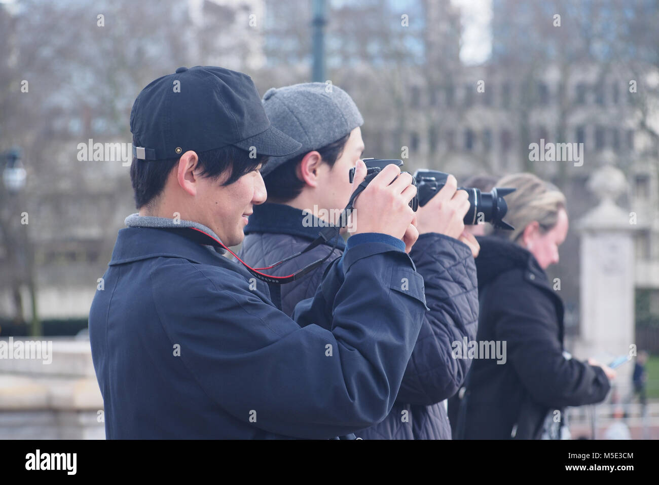 Deux jeunes hommes japonais à prendre des photos dans l'hiver du soleil dans l'avant-cour au palais de Buckingham portant des casquettes de baseball et de manteaux d'hiver Banque D'Images