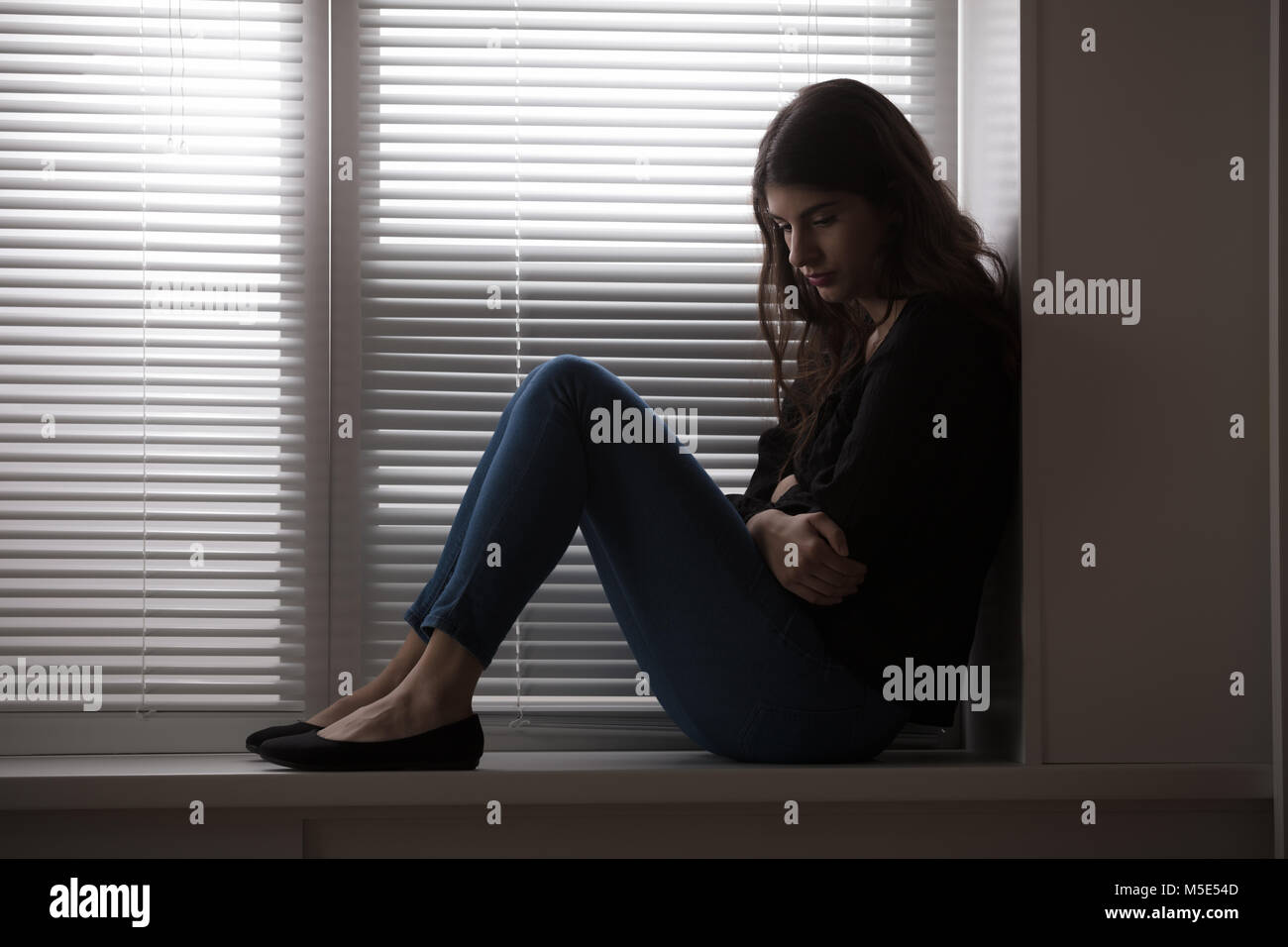 Jeune femme assise appuyée sur le rebord de la fenêtre Banque D'Images