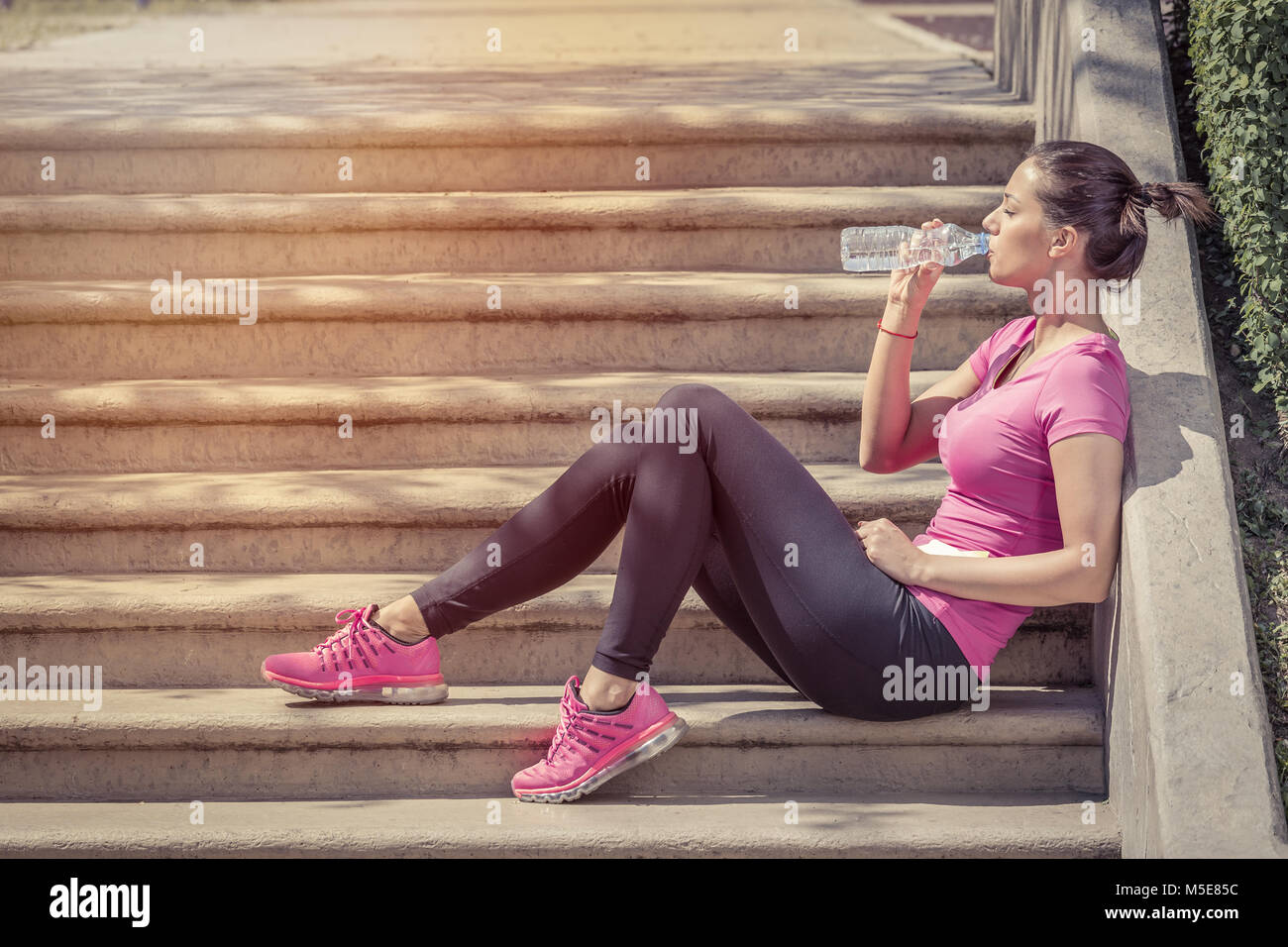 Runner Fitness femme l'eau potable et à l'assis sur un escalier. Fille de l'athlète en faisant une pause pendant l'exécution d'hydrater pendant les chaudes journées d'été. Vie saine et active Banque D'Images