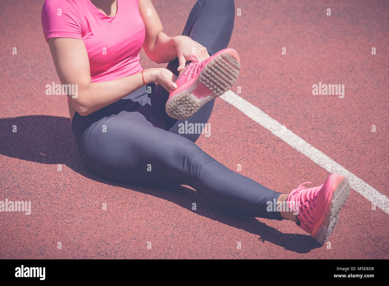 Female jogger mains sur pied. Elle ressent la douleur comme la cheville ou le pied est cassé ou tordu. Accident sur une piste de course au cours de l'exercice matinal. Spo Banque D'Images