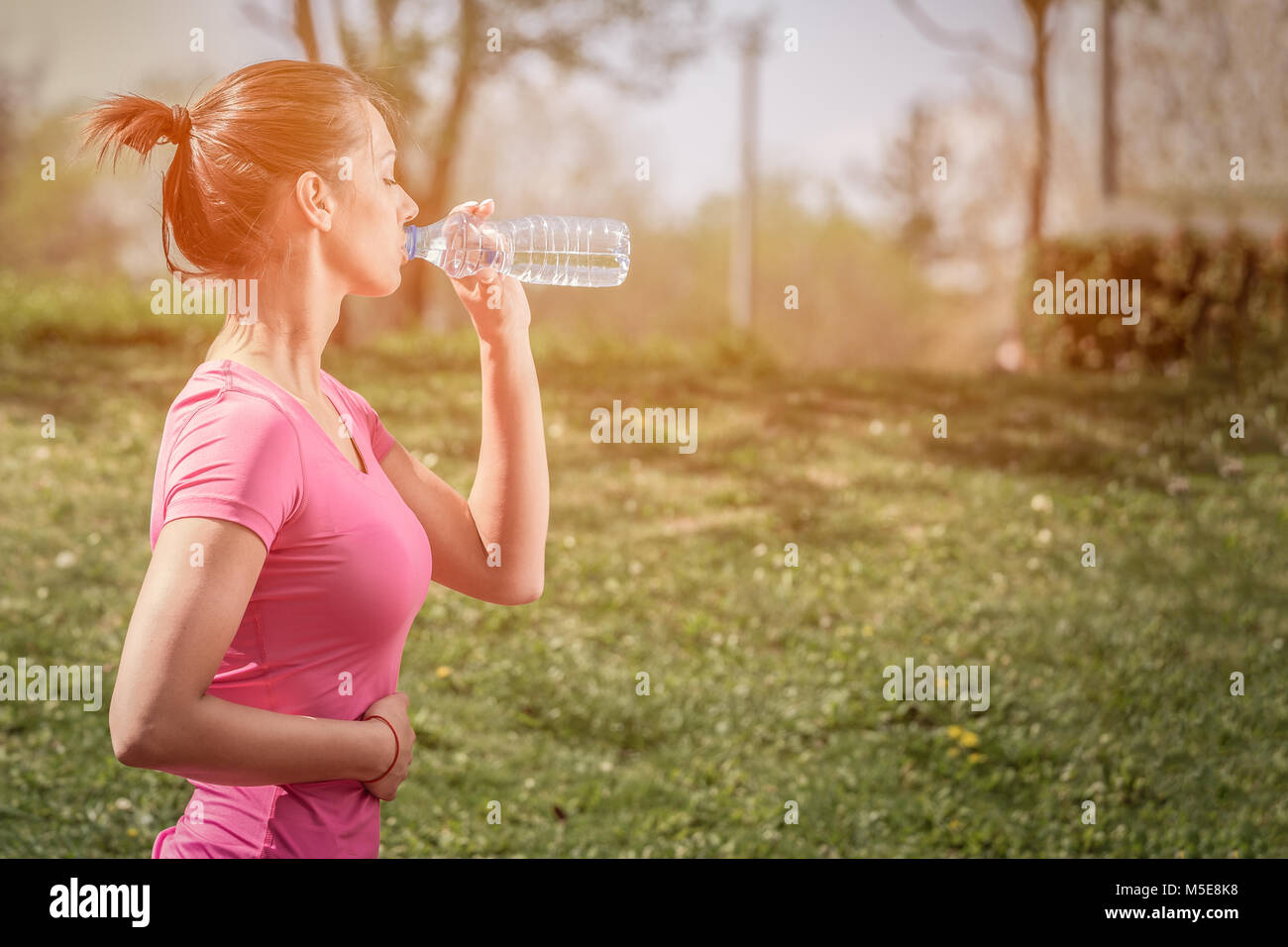 Runner Fitness Femme de l'eau potable dans le parc. Fille de l'athlète en faisant une pause pendant l'exécution d'hydrater pendant les chaudes journées d'été. Mode de vie sain et actif. Banque D'Images