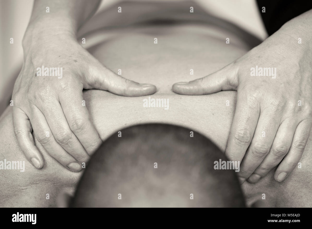 Une masseuse effectue un massage sur le haut du dos d'un client, un homme de race blanche horizontale de l'image en noir et blanc, sépia. Banque D'Images