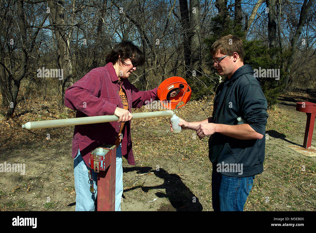 Emporia Kansas, États-Unis, 27 mars, 2014 Le Dr Marcia Schlumeister Professeur agrégé de sciences physiques et Bryce Wagoner un de ses étudiants utilisent une écope (un outil qui apporte de l'eau de puits pour échantillons) de prendre un échantillon d'eau à un puits d'essai sur le terrain de Emporia State University pour les tests de niveaux de concentration d'azote et de potassium. Banque D'Images