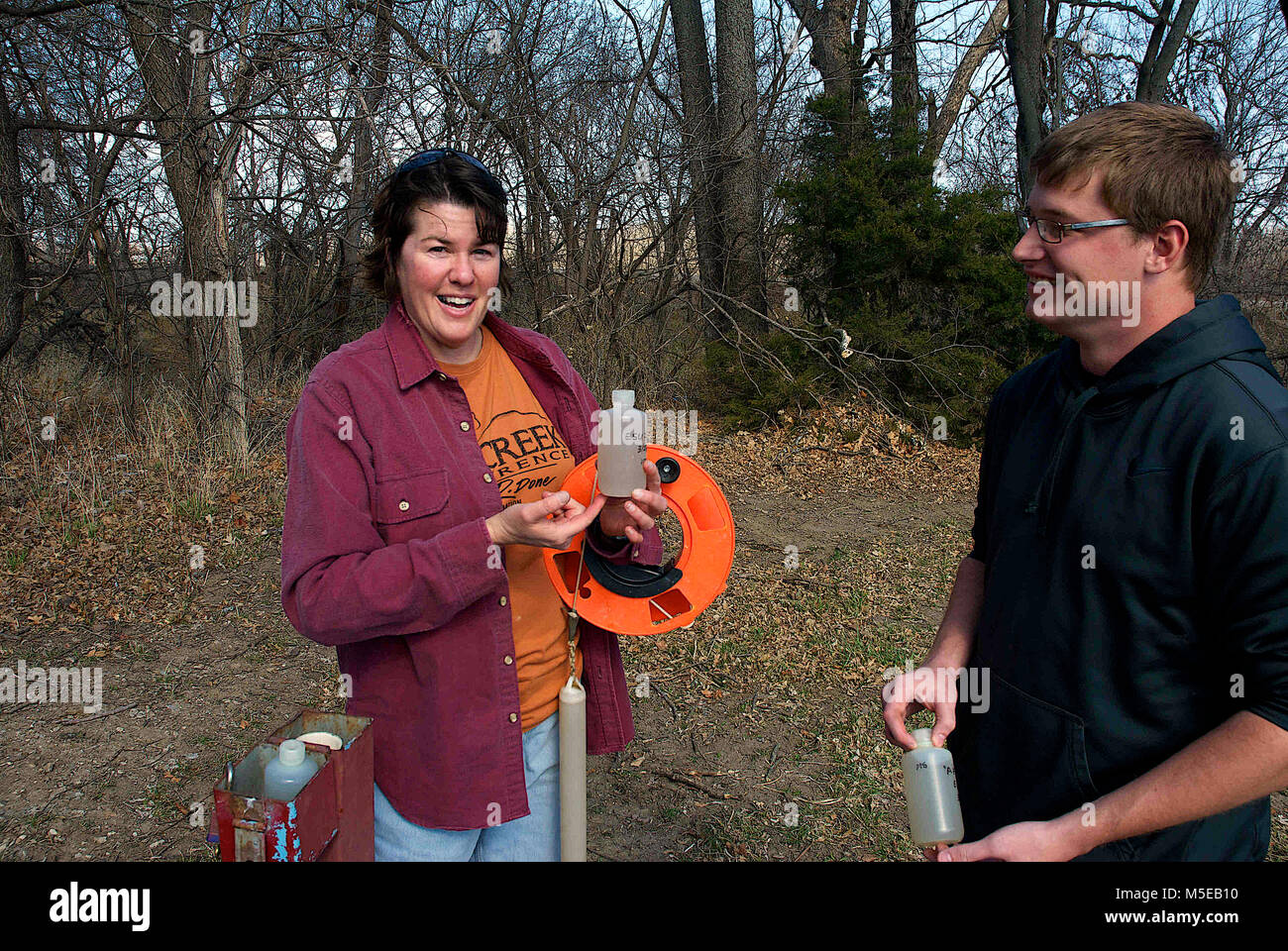 Emporia Kansas, États-Unis, 27 mars, 2014 Le Dr Marcia Schlumeister Professeur agrégé de sciences physiques et Bryce Wagoner un de ses étudiants utilisent une écope (un outil qui apporte de l'eau de puits pour échantillons) de prendre un échantillon d'eau à un puits d'essai sur le terrain de Emporia State University pour les tests de niveaux de concentration d'azote et de potassium. Banque D'Images