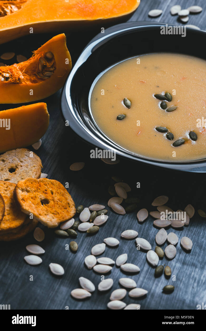 Soupe au potiron avec des tranches de citrouille fraîche sur un côté. Fond en bois foncé Banque D'Images