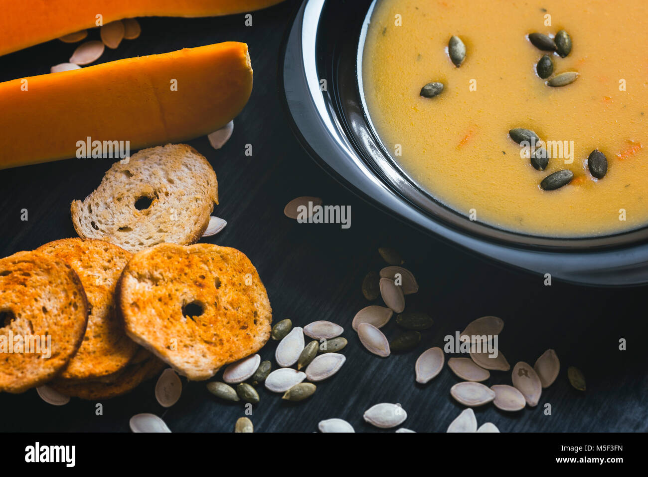 Soupe au potiron avec des tranches de citrouille fraîche sur un côté. Fond en bois foncé Banque D'Images