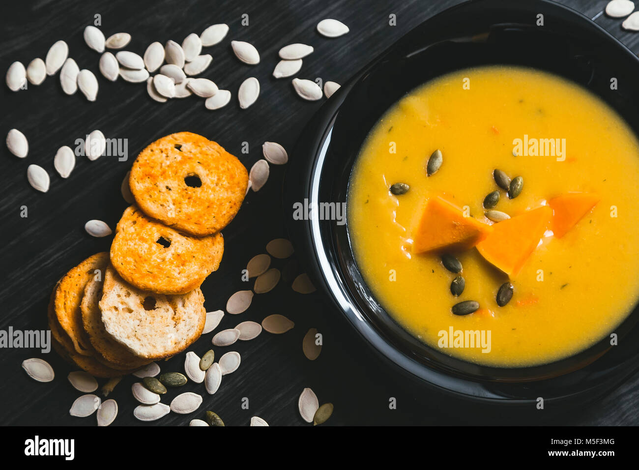 Soupe au potiron avec des tranches de citrouille fraîche sur un côté. Fond en bois foncé Banque D'Images