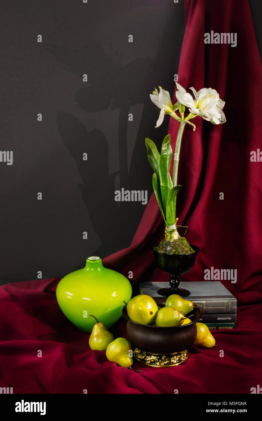 Encore une vie de poires, une fleur, un vase et composée de livres verts et jaunes contraste sur un fond drapé rouge. Banque D'Images