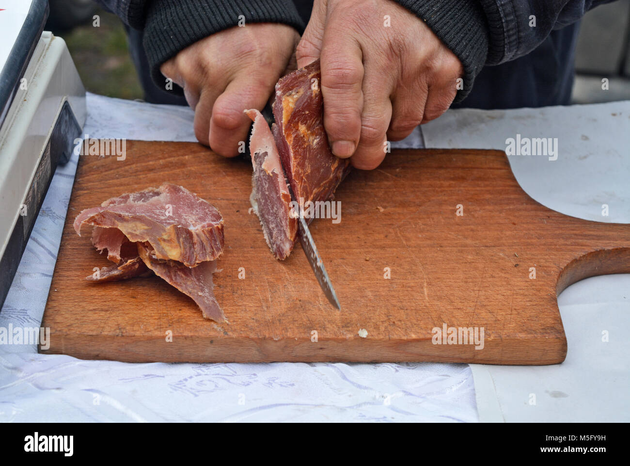 Un homme avec un couteau coupe des morceaux de jambon séché et fumé pour la dégustation. Banque D'Images Un homme avec un couteau coupe des morceaux de jambon séché et fumé pour la dégustation. Banque D'Images