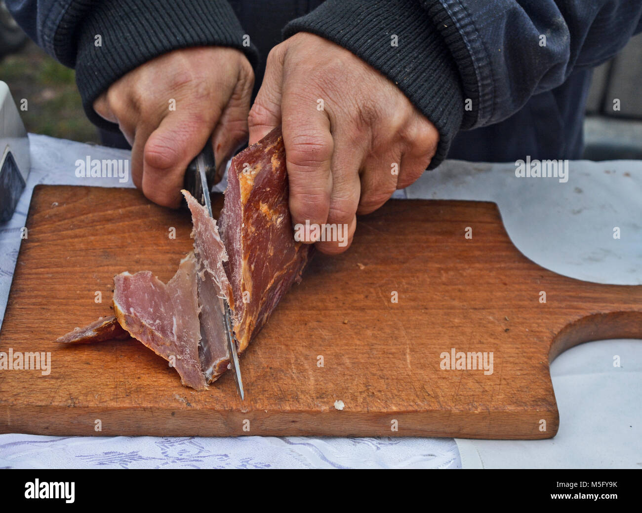 Un homme avec un couteau coupe des morceaux de jambon séché et fumé pour la dégustation. Banque D'Images Un homme avec un couteau coupe des morceaux de jambon séché et fumé pour la dégustation. Banque D'Images