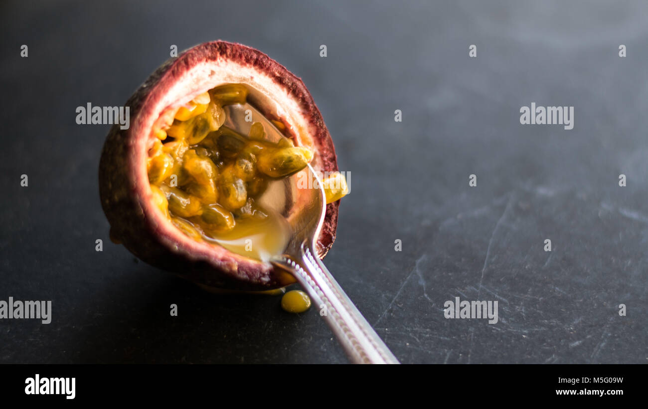 Delicious fresh fruit juteux, maracuja moitié avec spoon gros plan, arrière-plan sombre. La moitié de la passion bien mûrs, granadilla, chair jaune, des graines noires. Banque D'Images