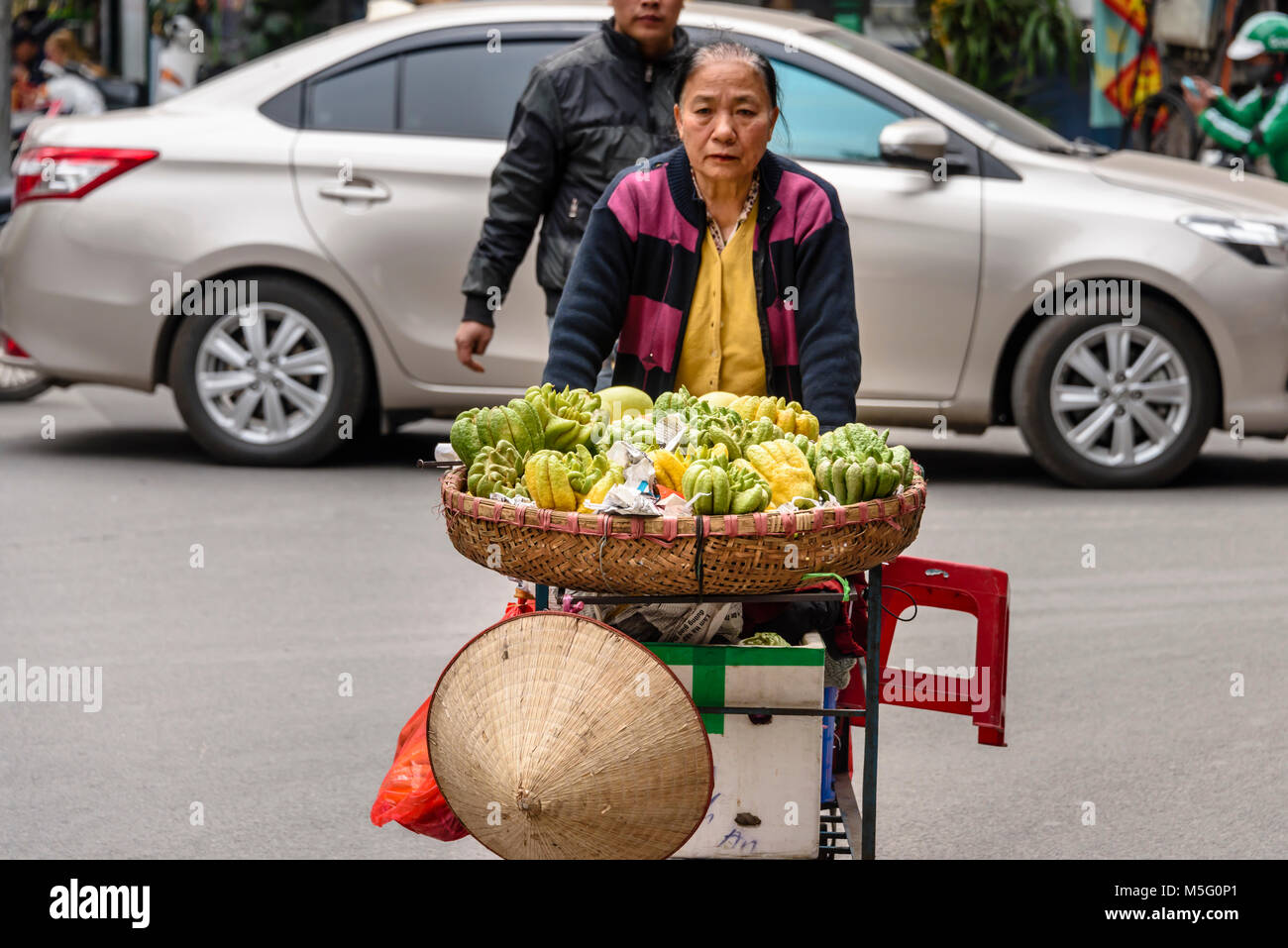 Une vietnamienne pousse sa charrette à base de fruits le long d'une rue à Hanoi, Vietnam. Banque D'Images