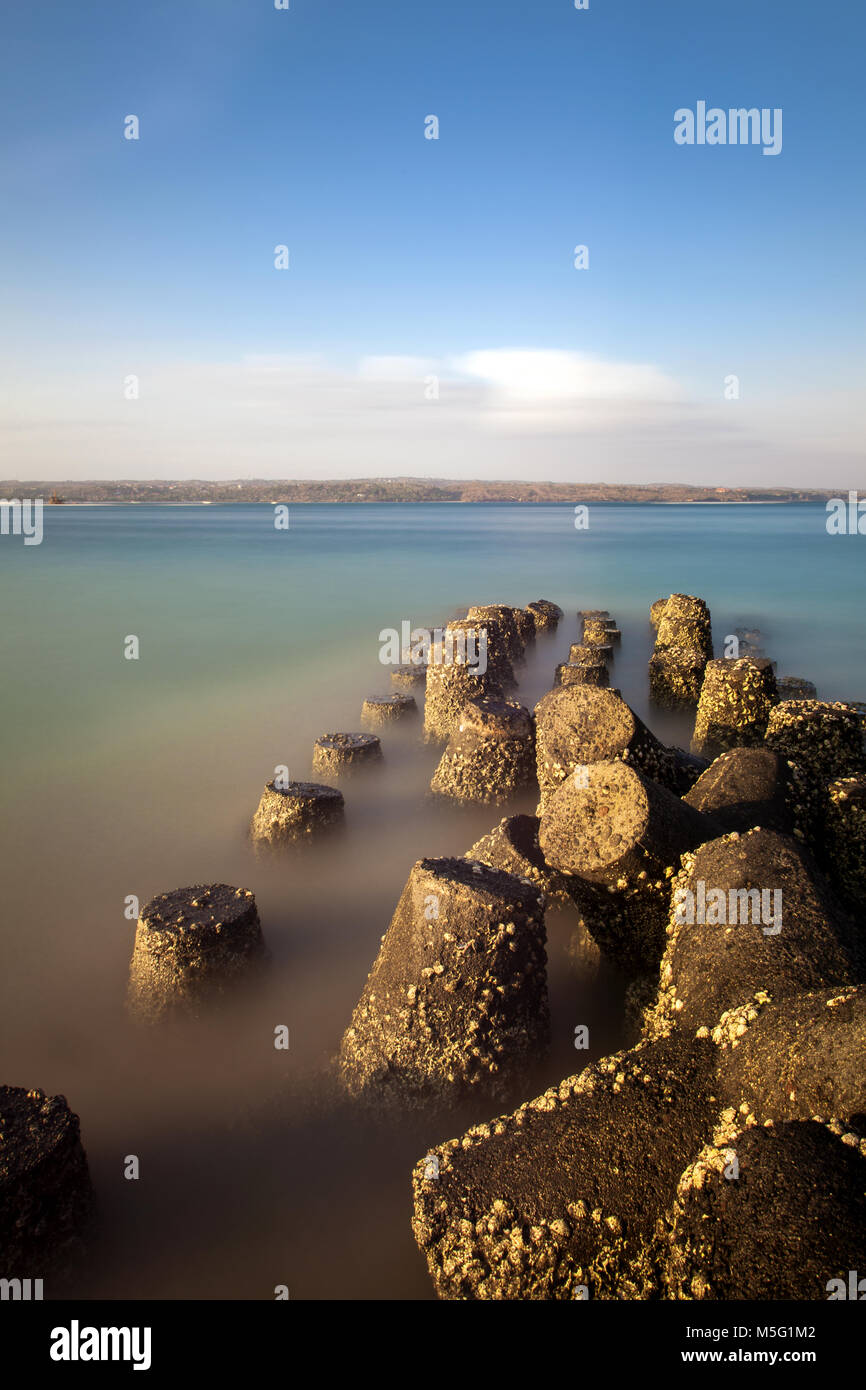 Les défenses maritimes concrètes sous forme de tétrapodes à quatre pattes avec vue imprenable sur la mer et la terre d'en face sur l'horizon. L'exposition longue lisse de l'image de mer Banque D'Images