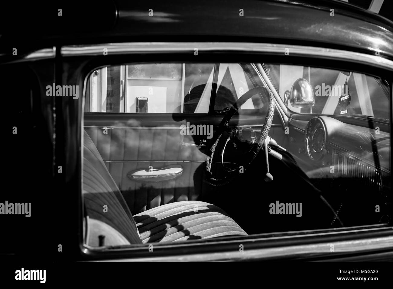 La réflexion monochrome d'un homme dans une voiture Chevrolet vintage. Banque D'Images