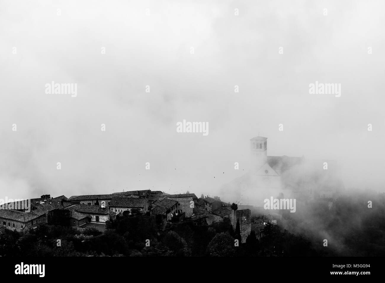 Voir l'église Papale de Saint François à Assise (Ombrie, Italie) au milieu de la levée matin brouillard, avec quelques oiseaux volant Banque D'Images