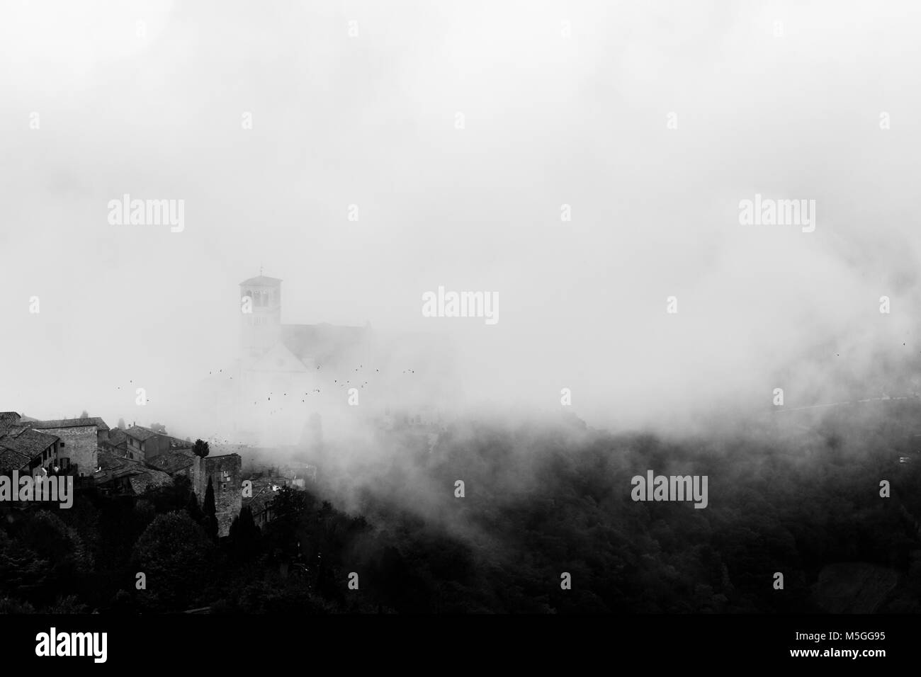 Voir l'église Papale de Saint François à Assise (Ombrie, Italie), dans le milieu de la levée du brouillard du matin avec quelques oiseaux volant Banque D'Images