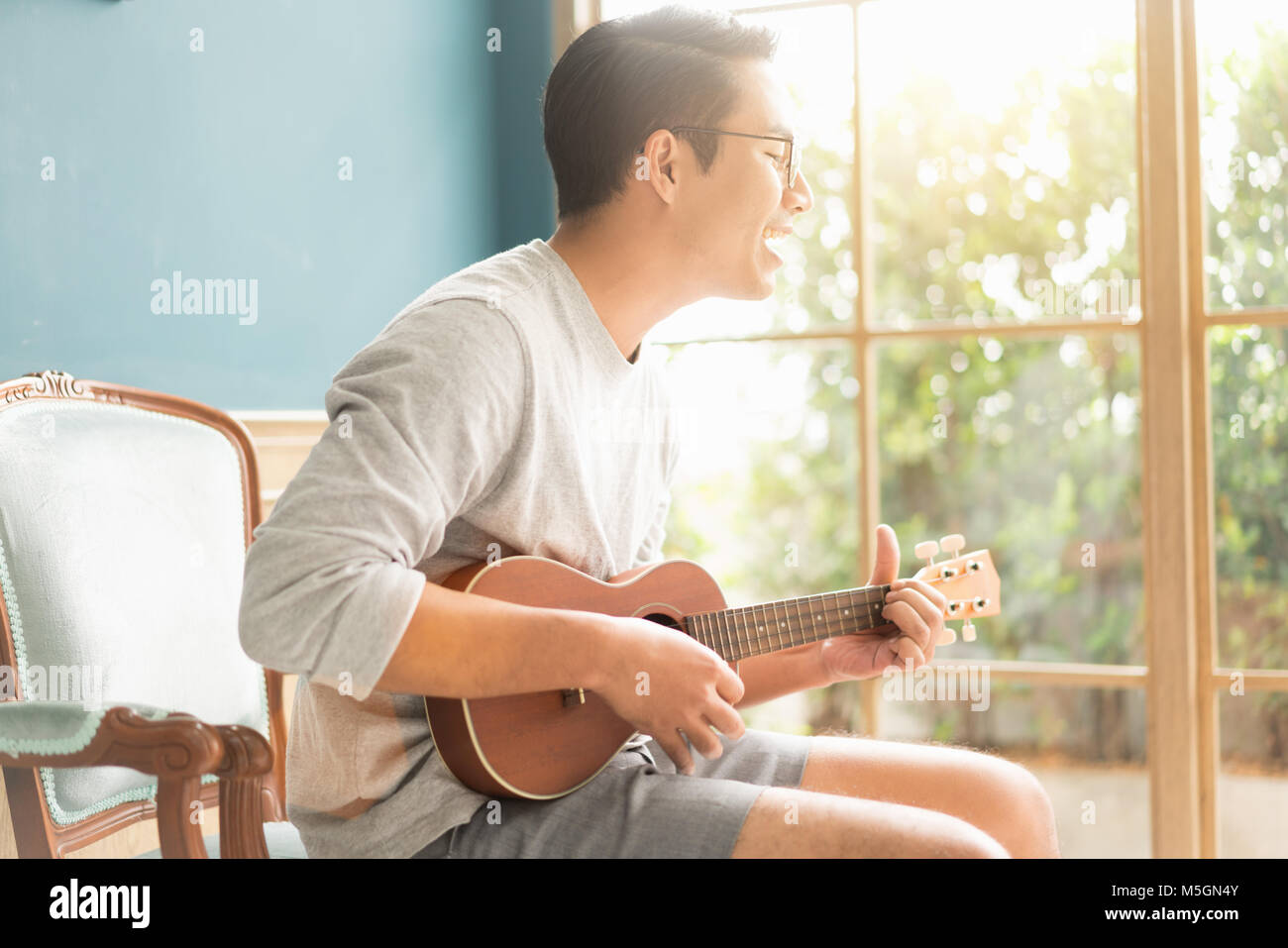 Asian young man hands playing acoustic guitar ukulele à la maison. Profitez de jouer la guitare acoustique de soleil dans la soirée. Banque D'Images