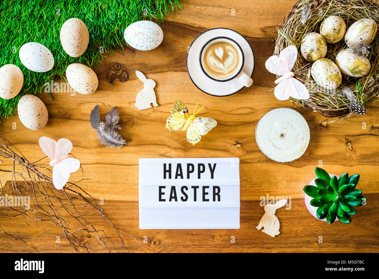 Tourné à partir de ci-dessus comme flatlay avec Happy Easter message écrit sur caisson lumineux et colorés des oeufs de pâques rétro, l'herbe, papillon et nid de Pâques sur des t Banque D'Images