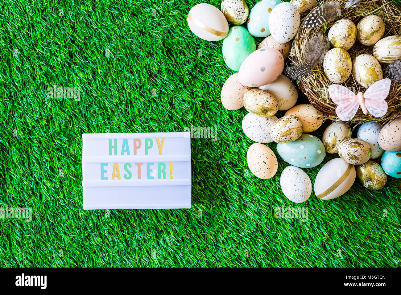 Tourné à partir de ci-dessus comme flatlay avec Happy Easter message écrit sur caisson lumineux et colorés des oeufs de pâques rétro, l'herbe, papillon et nid de Pâques Banque D'Images