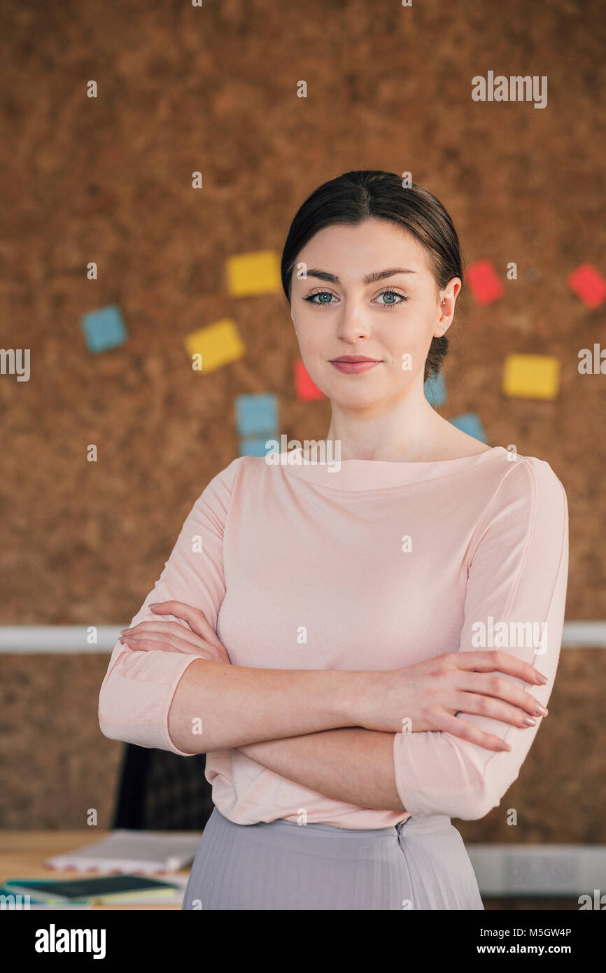 Portrait of a female office worker. Elle est debout devant un panneau de liège, smartly dressed avec ses bras croisés et sourit pour la photo. Banque D'Images