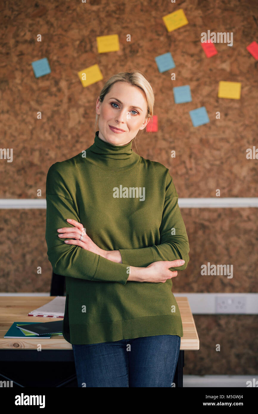 Portrait of a female office worker. Elle est debout devant un panneau de liège, smartly dressed avec ses bras croisés et sourit pour la photo. Banque D'Images