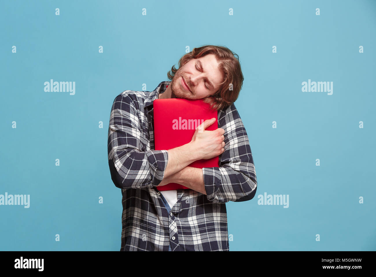 Businessman hugging ordinateur portable. L'amour à computer concept. Attractive male avant mi-longueur à la mode, portrait studio bleu backgroud. Les jeunes bearde émotionnelle Banque D'Images