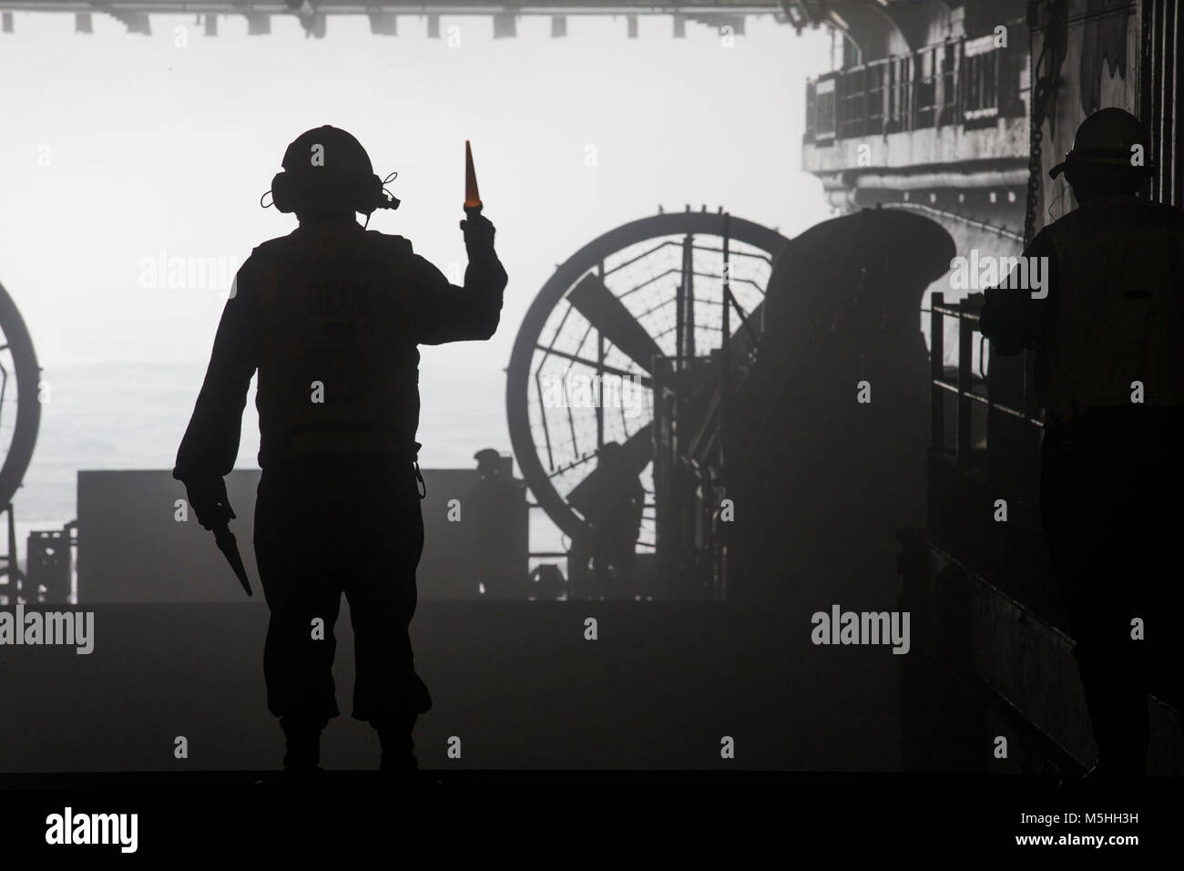 Un marin de la marine américaine avec l'Iwo Jima Groupe amphibie (ARG), le signal d'un Landing Craft Air Cushion (LCAC) à quitter le pont du coffre du navire d'assaut amphibie USS Iwo Jima (DG 7), le 11 février 2018. L'ARG/26e Marine Expeditionary Unit (MEU) équipe déploie en mer pour mener des opérations de sécurité maritime, d'intervention en cas de crise et le théâtre de la coopération en matière de sécurité, tout en offrant une présence navale expéditionnaire en Europe et au Moyen-Orient. (U.S. Marine Corps Banque D'Images