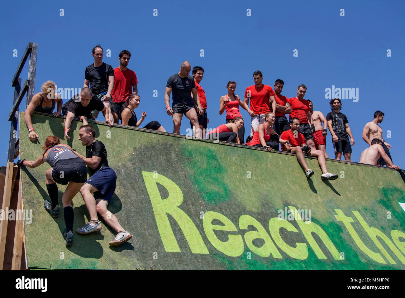 Une équipe est d'aider leur coéquipier d'escalader un mur dans une course Run Légion force tenue à Sofia, Bulgarie le 26 juillet 2014 Banque D'Images